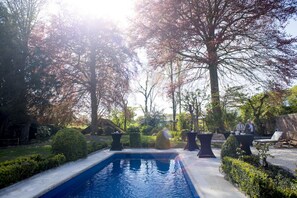 A swimming pool surrounded by neatly trimmed hedges and trees, with outdoor seating areas and a stone wall in the background. - B&B Filemon & Baucis (Bruges)
