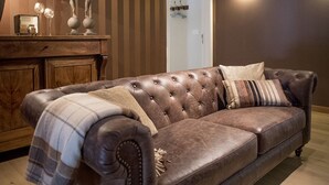A brown leather sofa with a plaid throw blanket, a wooden cabinet with decorative items, and a striped wall. - B&B Filemon & Baucis (Bruges)