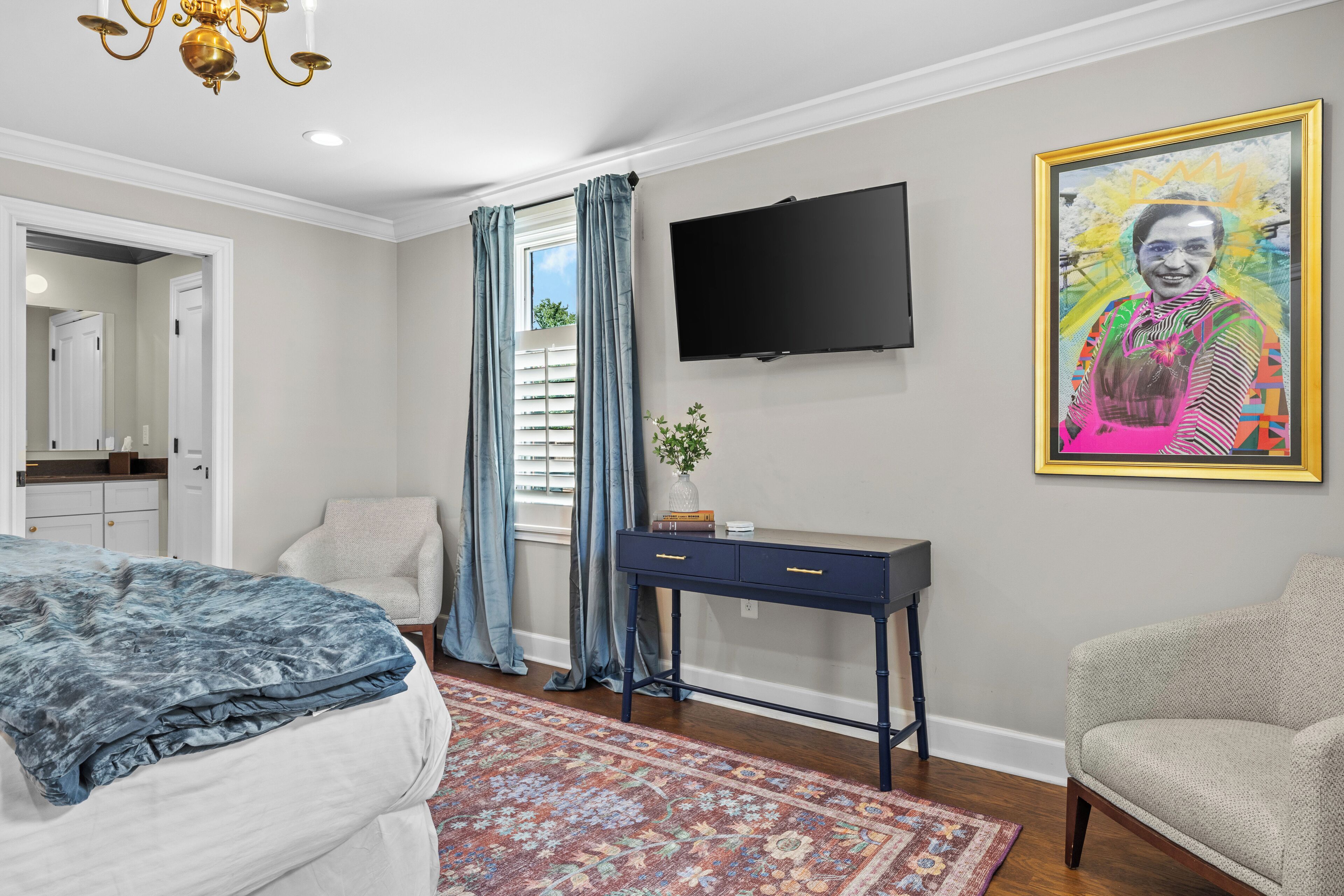 A bedroom with a bed, a desk, a chair, a television, and a painting on the wall.