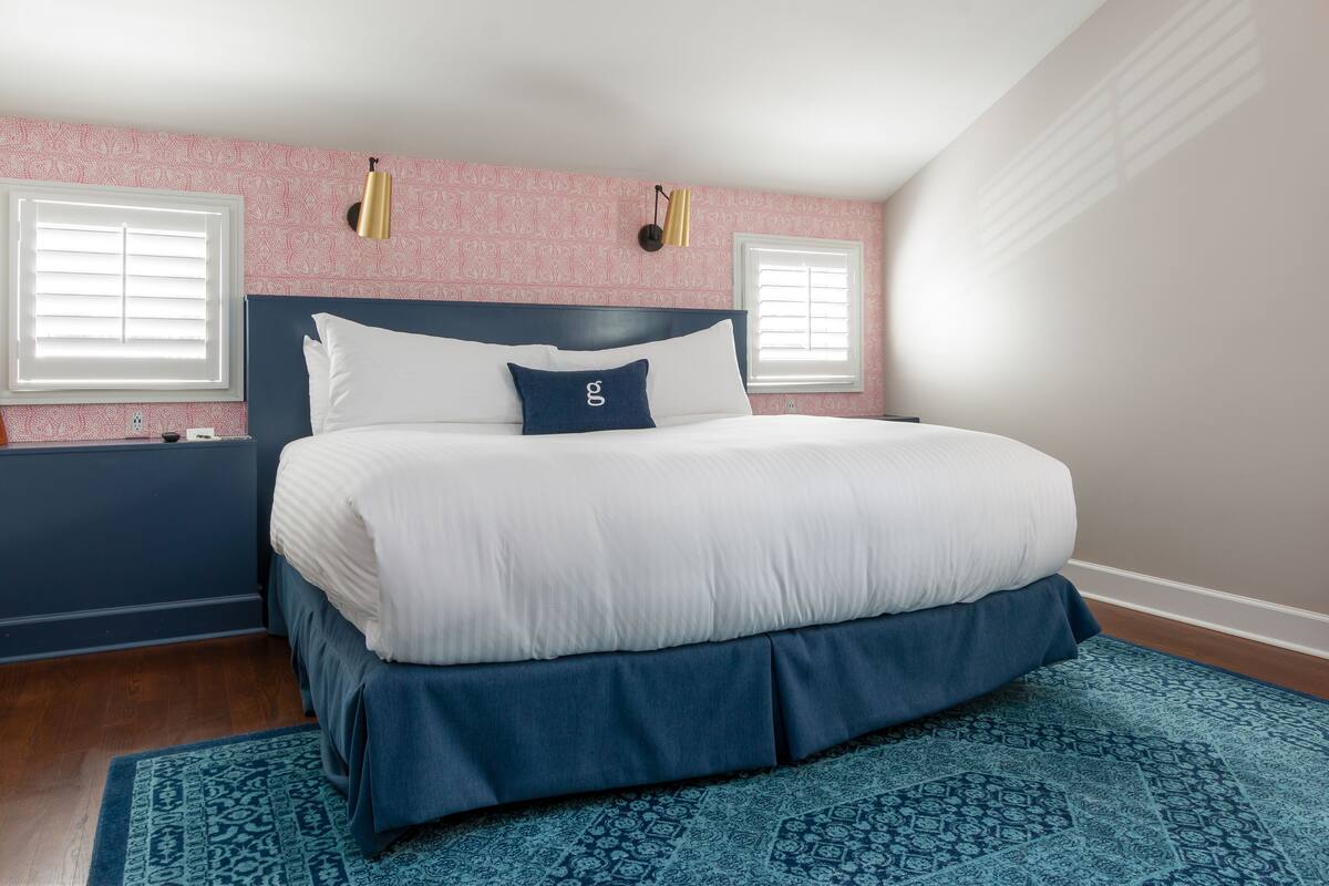 A bedroom with a large bed, a patterned wall, and a window with blinds.