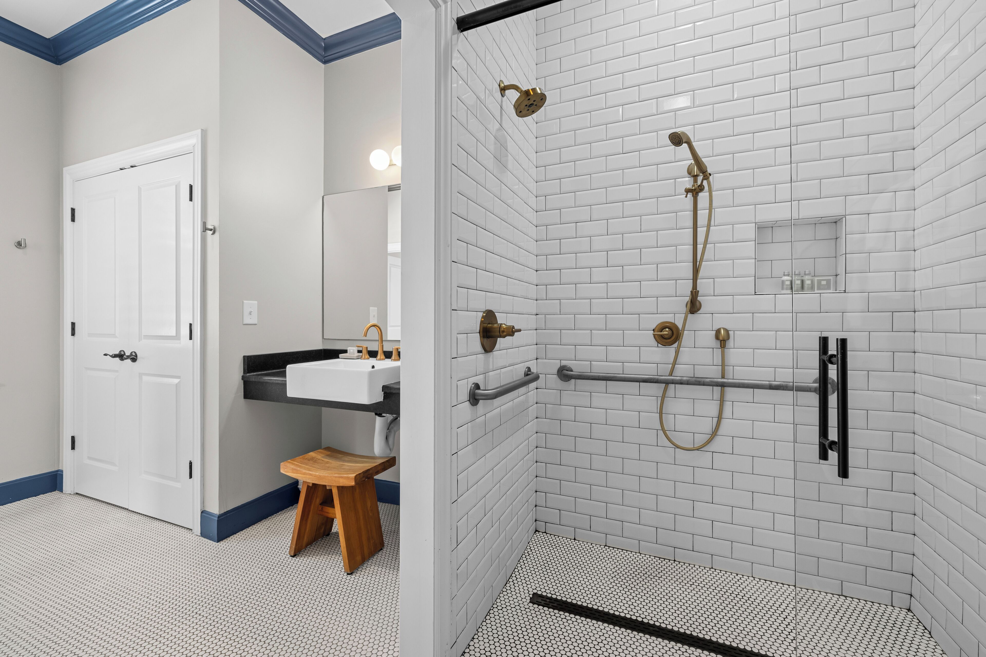 Un bagno con piastrelle bianche stile metro, una doccia con soffione manuale e un piccolo sgabello di legno.