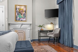 Una habitación de hotel con cama, escritorio y silla, televisor, chimenea y un amplio ventanal con cortinas.