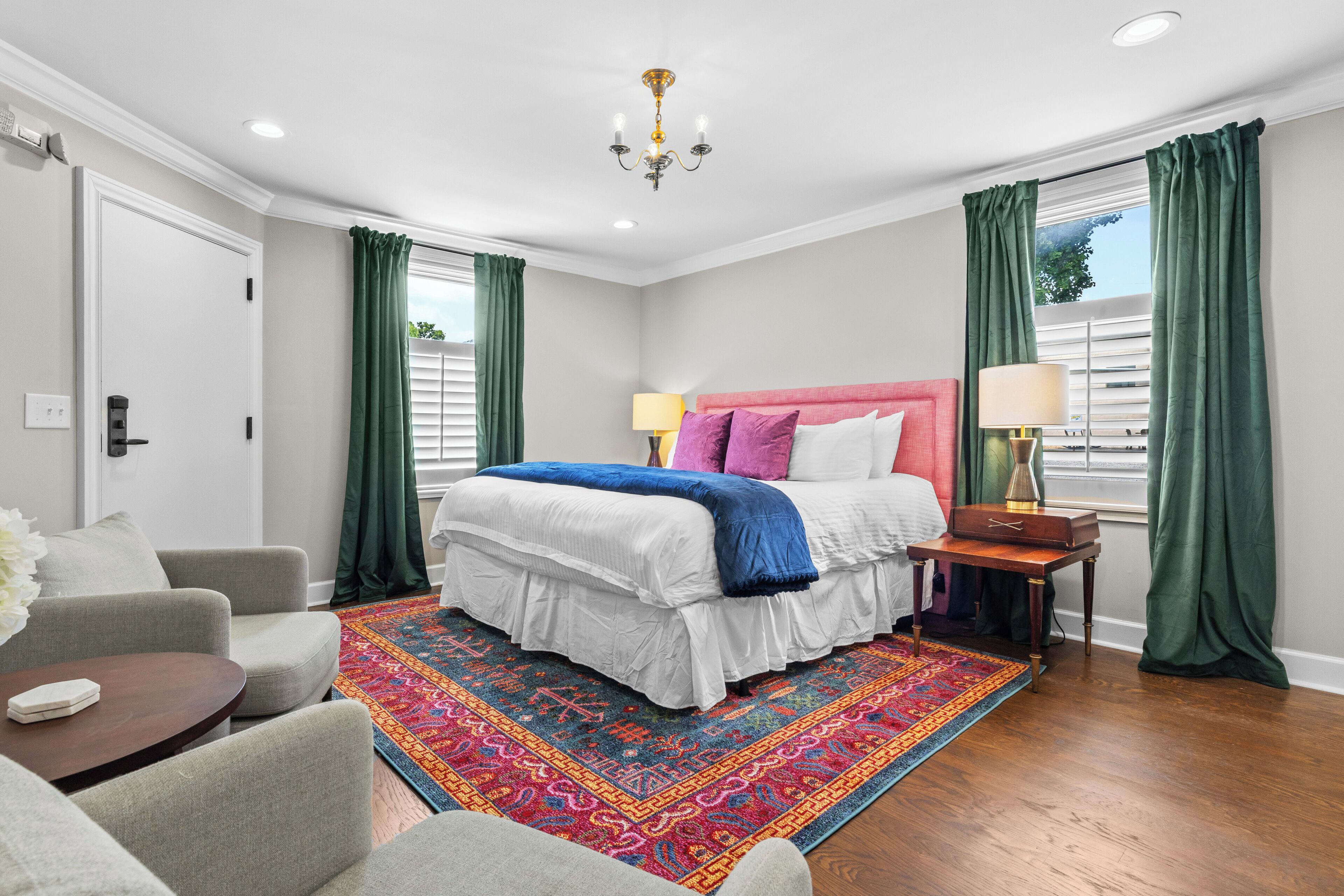 Un dormitorio con cama, mesita de noche, una silla, alfombra y ventana con cortinas.