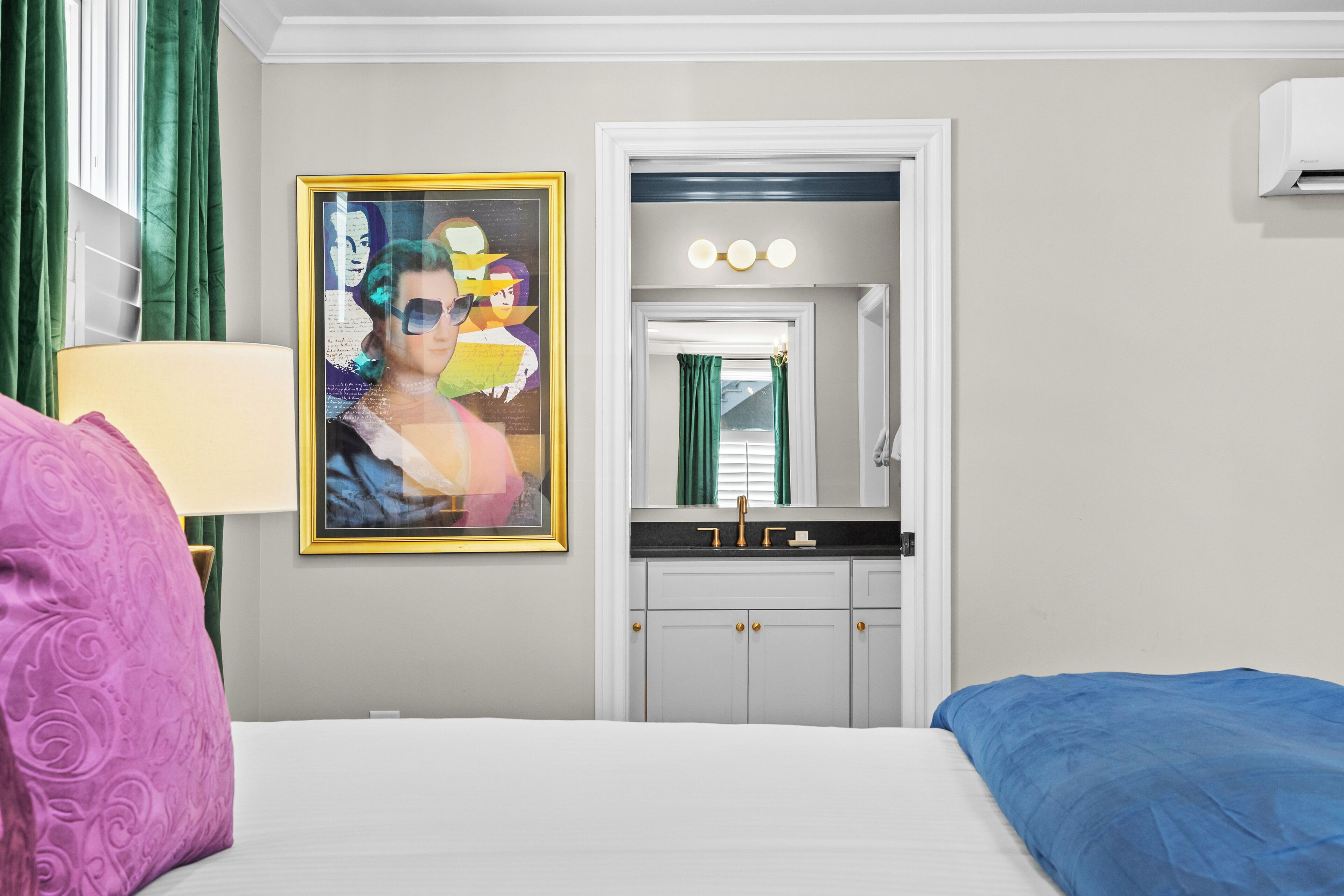 A hotel room with a bed, a nightstand, a mirror, a sink, and a window with curtains.
