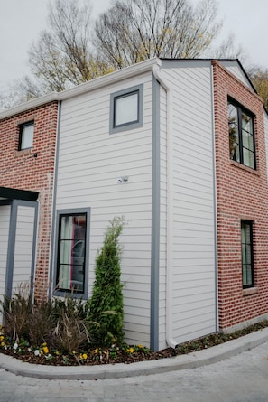 A two-story building with a combination of white siding and red brickwork, featuring a small window and a door on the ground floor.