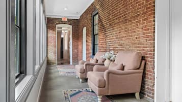 A hallway with brick walls, a white door, and a window. There are two armchairs with a vase of flowers on the floor.