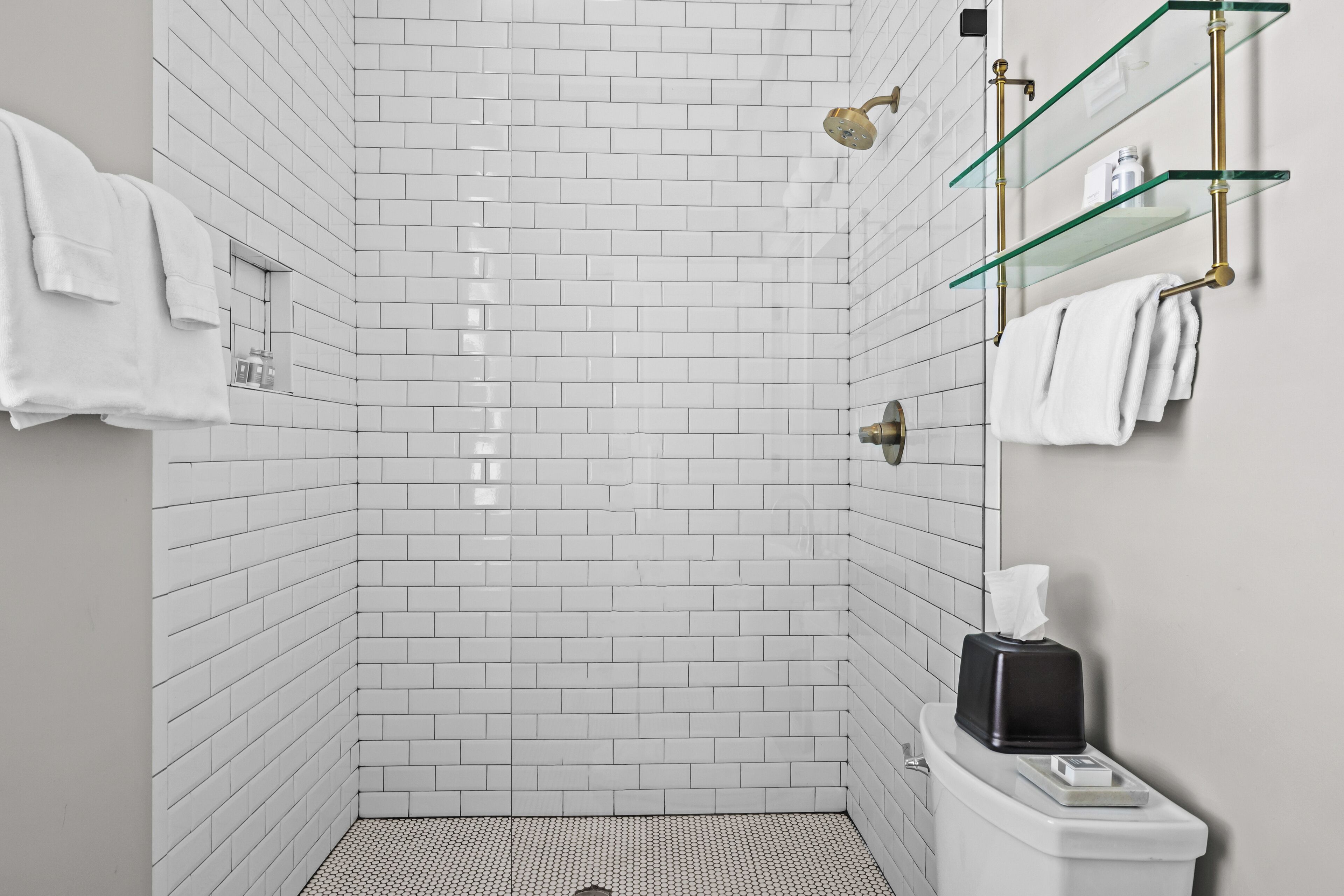 A modern bathroom with white subway tiles, a glass shower enclosure, and a toilet with a tissue box.