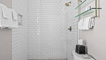 A modern bathroom with white subway tiles, a glass shower enclosure, and a toilet with a tissue box.