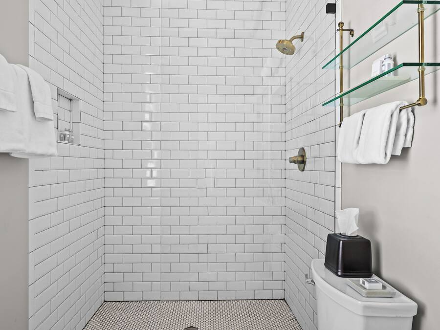 A modern bathroom with white subway tiles, a glass shower enclosure, and a toilet with a tissue box.