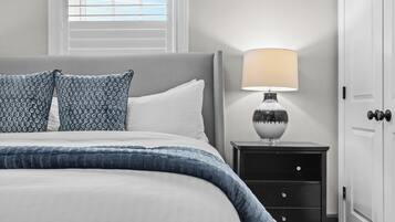 Una cama bien hecha con un cojín de diseño azul y blanco, una lámpara de noche y una mesita de noche con cajones.