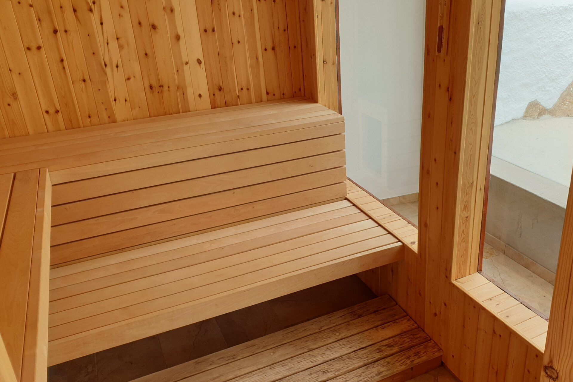 A wooden bench with horizontal slats, positioned against a wall with a window.
