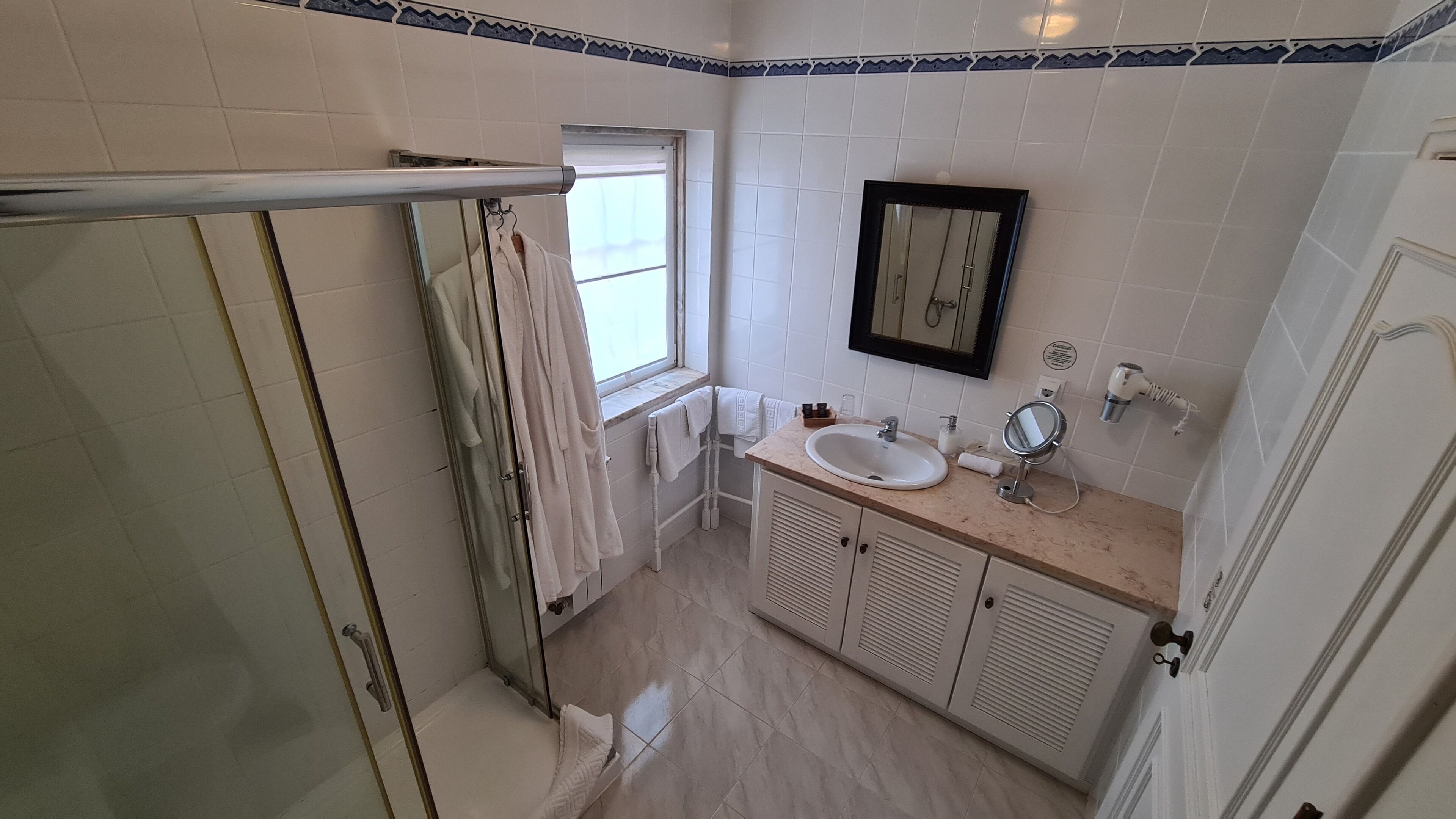 A bathroom with a shower, a sink, a mirror, and a window.