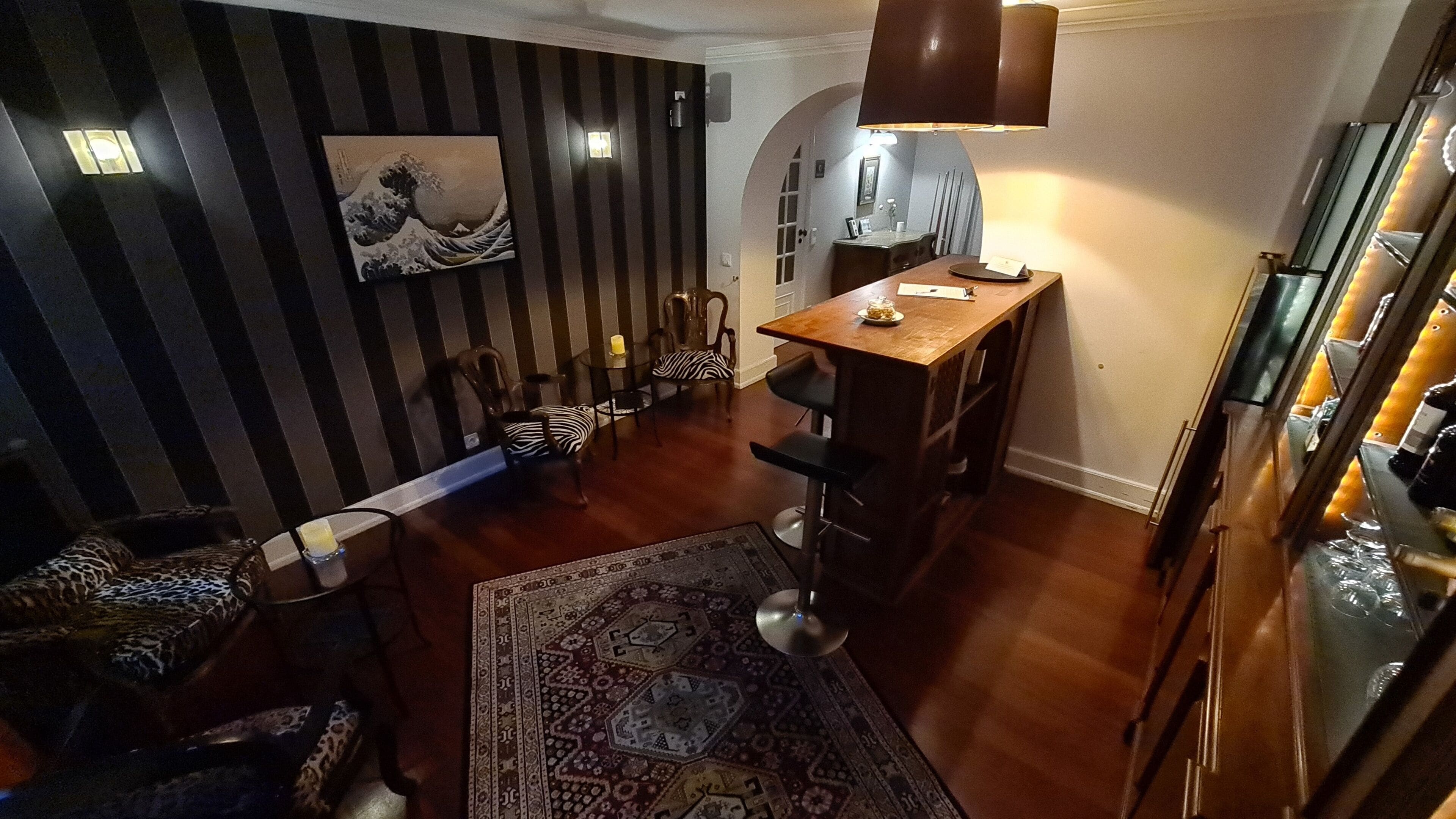 A dining area with a wooden table and chairs, a patterned rug, and a wall-mounted painting.