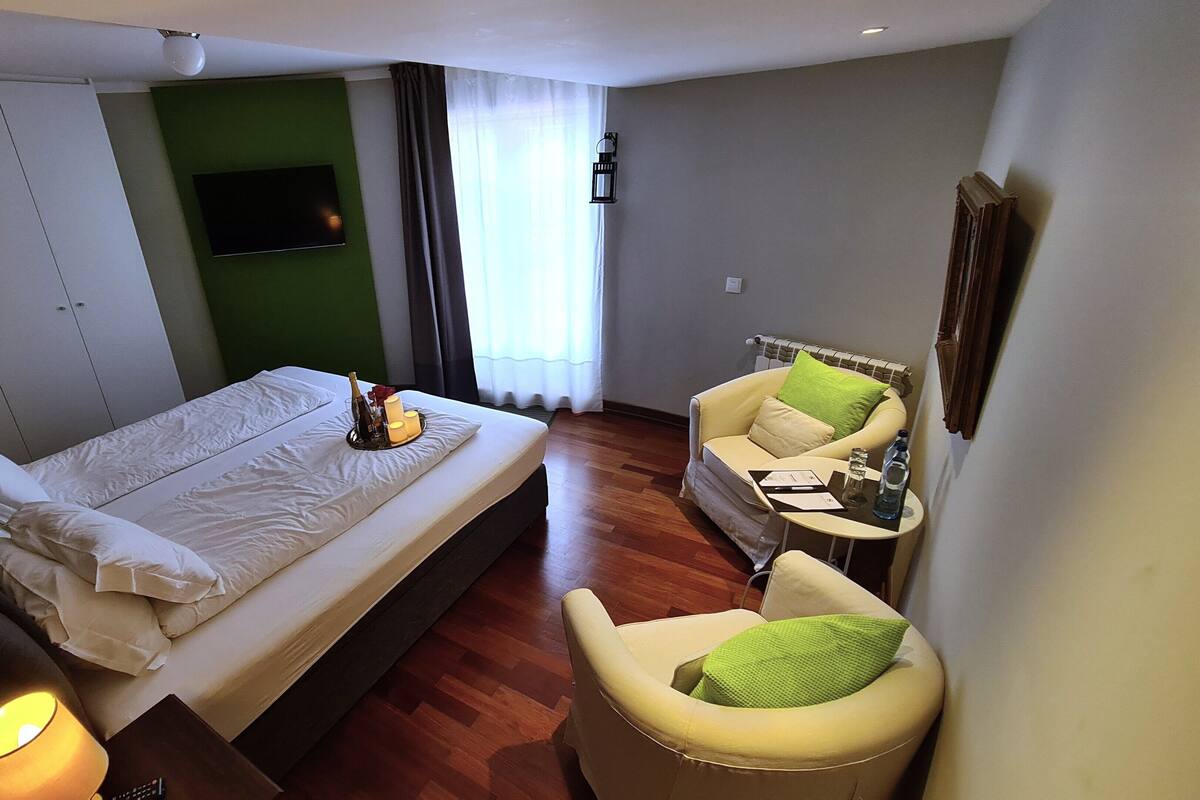 Una habitació d'hotel amb un llit, un sofà, una taula petita i una televisió penjada a la paret.