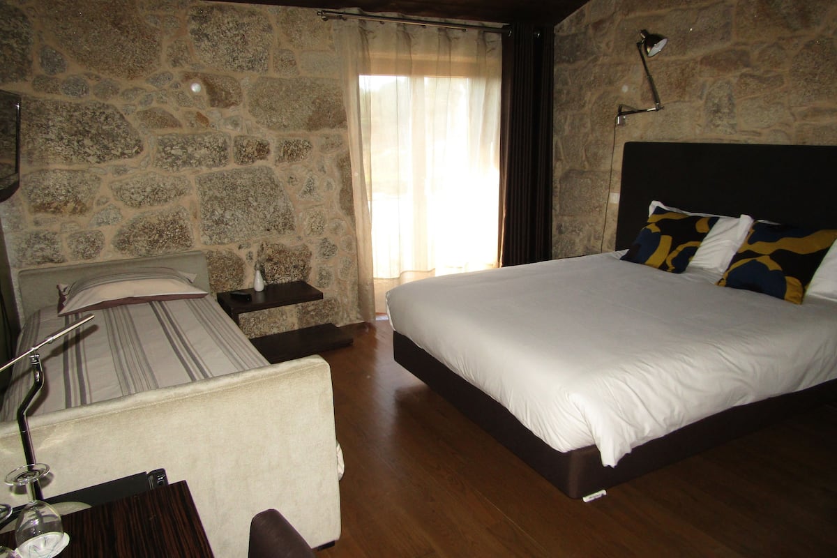 A bedroom with a stone wall, a bed with white bedding, a bedside table, and a lamp.