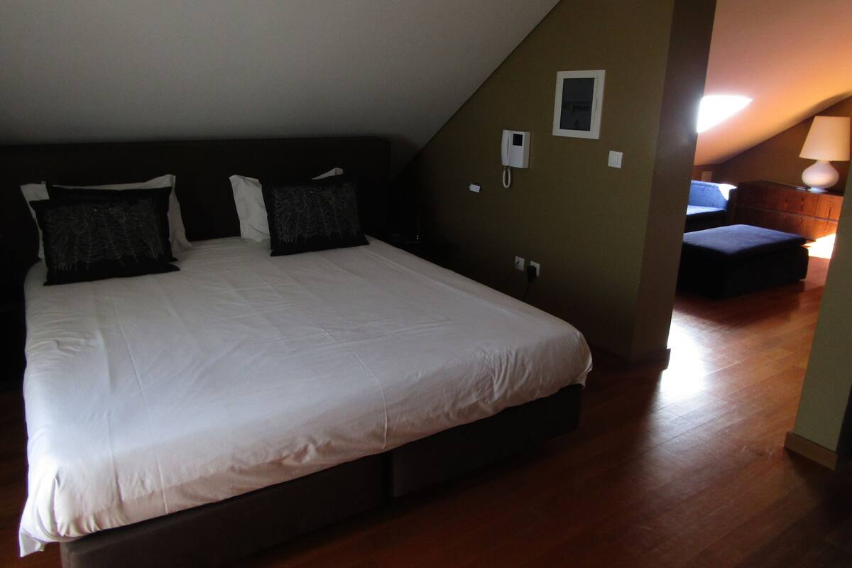 A bedroom with a large bed, a bedside table, a lamp, and a small chair.