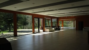 Espai interior ampli amb portes de vidre grans que donen a un jardí, bigues de fusta al sostre i zona de seients amb sofàs.