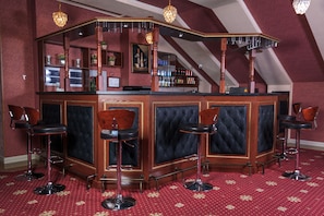 Eine Bar mit hoher, gewölbter Decke und rotem Teppichboden. Vier Barhocker und eine Bar mit schwarzer Polsterlehne sind vorhanden.