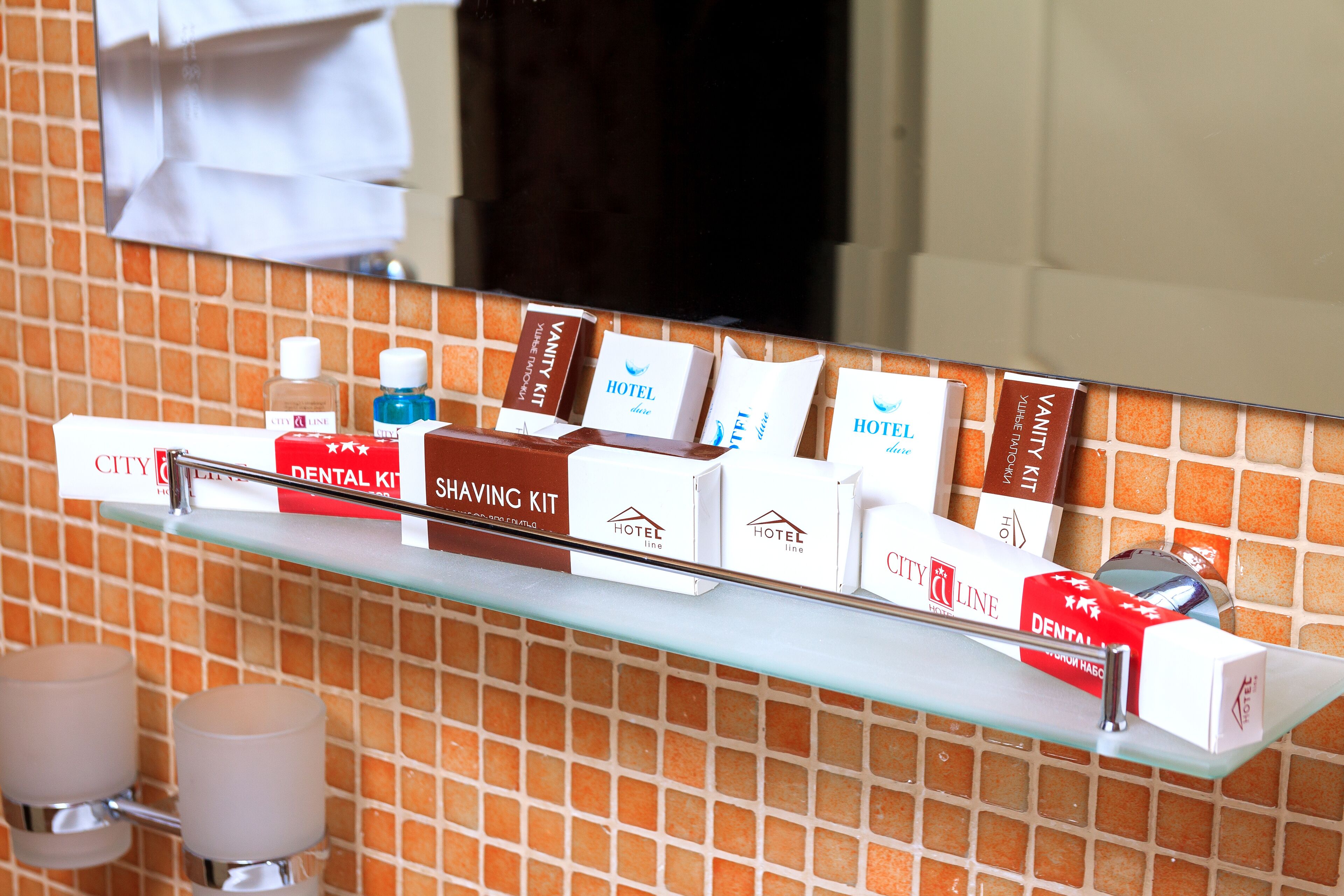 A hotel reception area with a glass shelf displaying various amenities including a dental kit, shaving kit, and hotel-branded boxes.