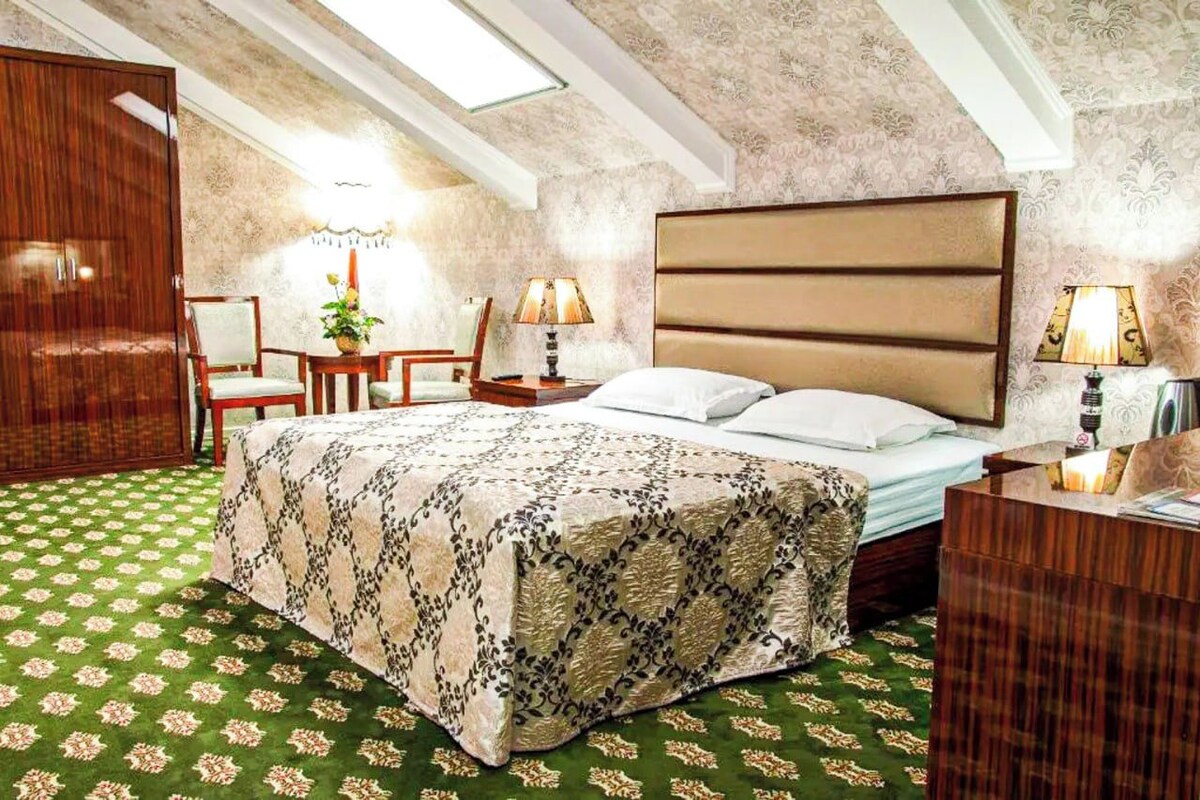 A bedroom with a large bed, two bedside tables, a wooden wardrobe, and a skylight.