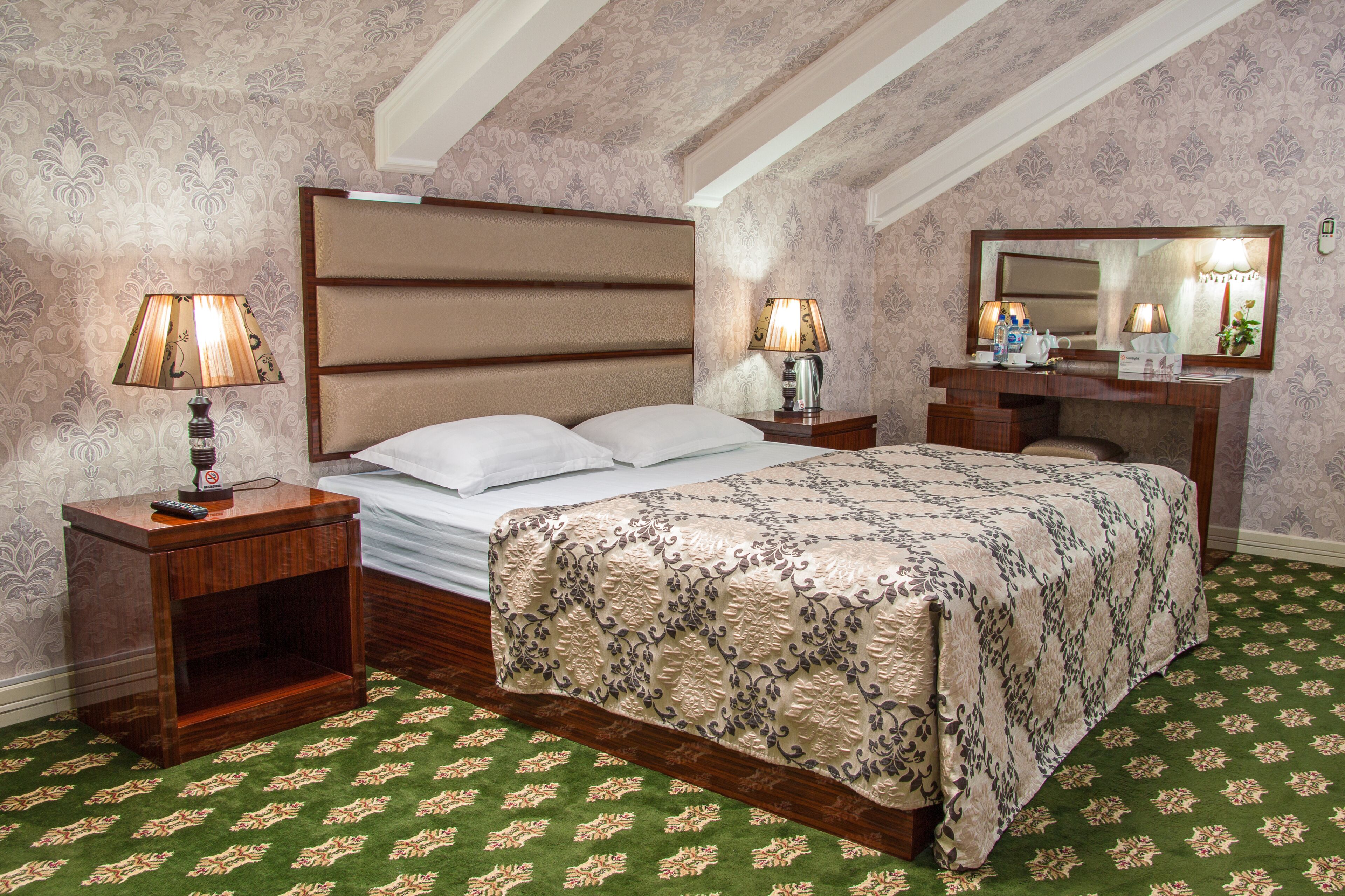 A bedroom with a large bed, two bedside tables with lamps, a dresser, and a mirror.