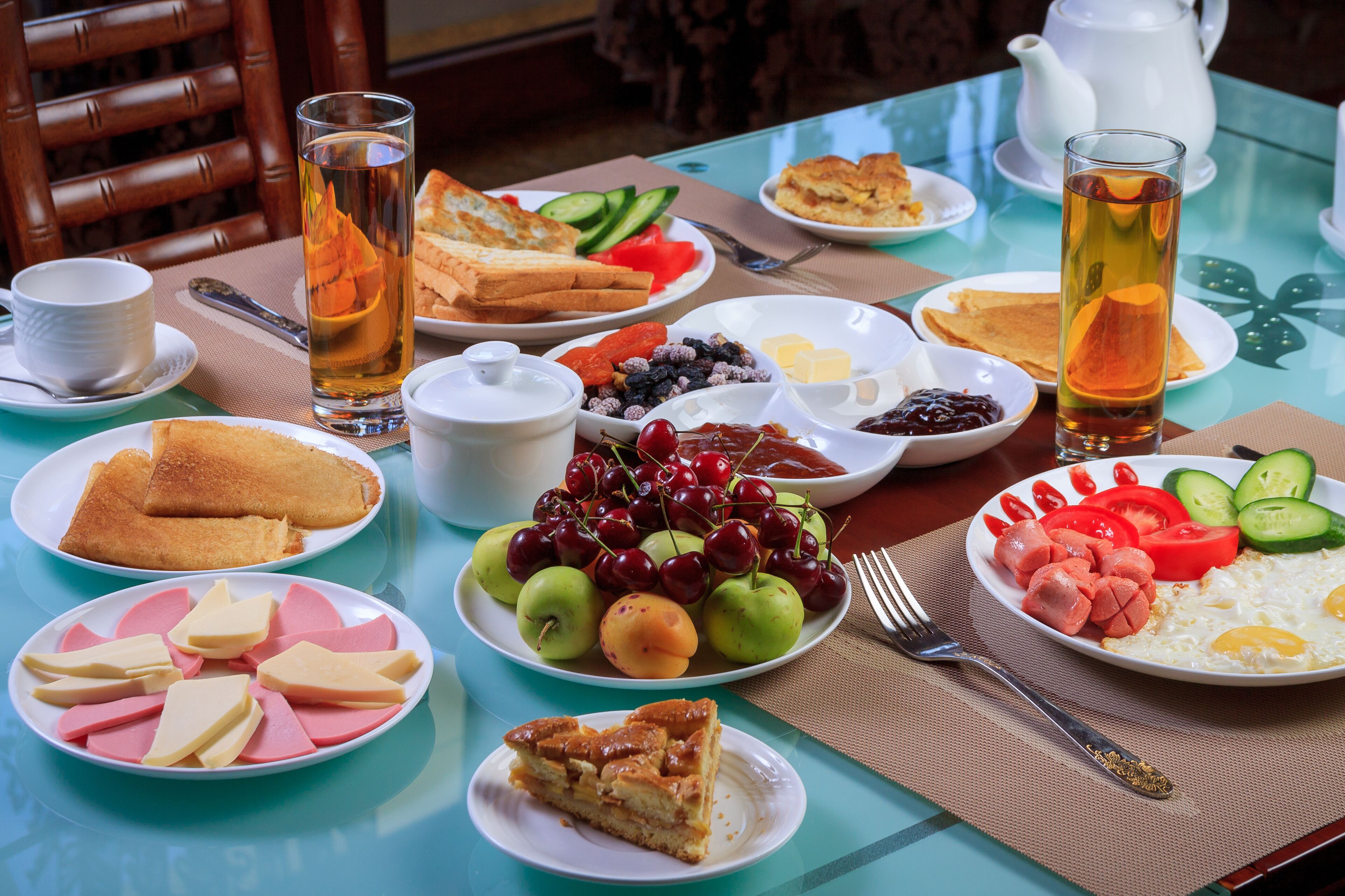 Mesa de café da manhã com diversos pratos, incluindo torradas, frutas, ovos e bebidas.