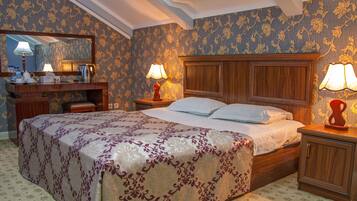 Habitación de hotel con una cama grande, cabecera de madera, dos mesitas de noche con lámparas, cómoda y espejo.