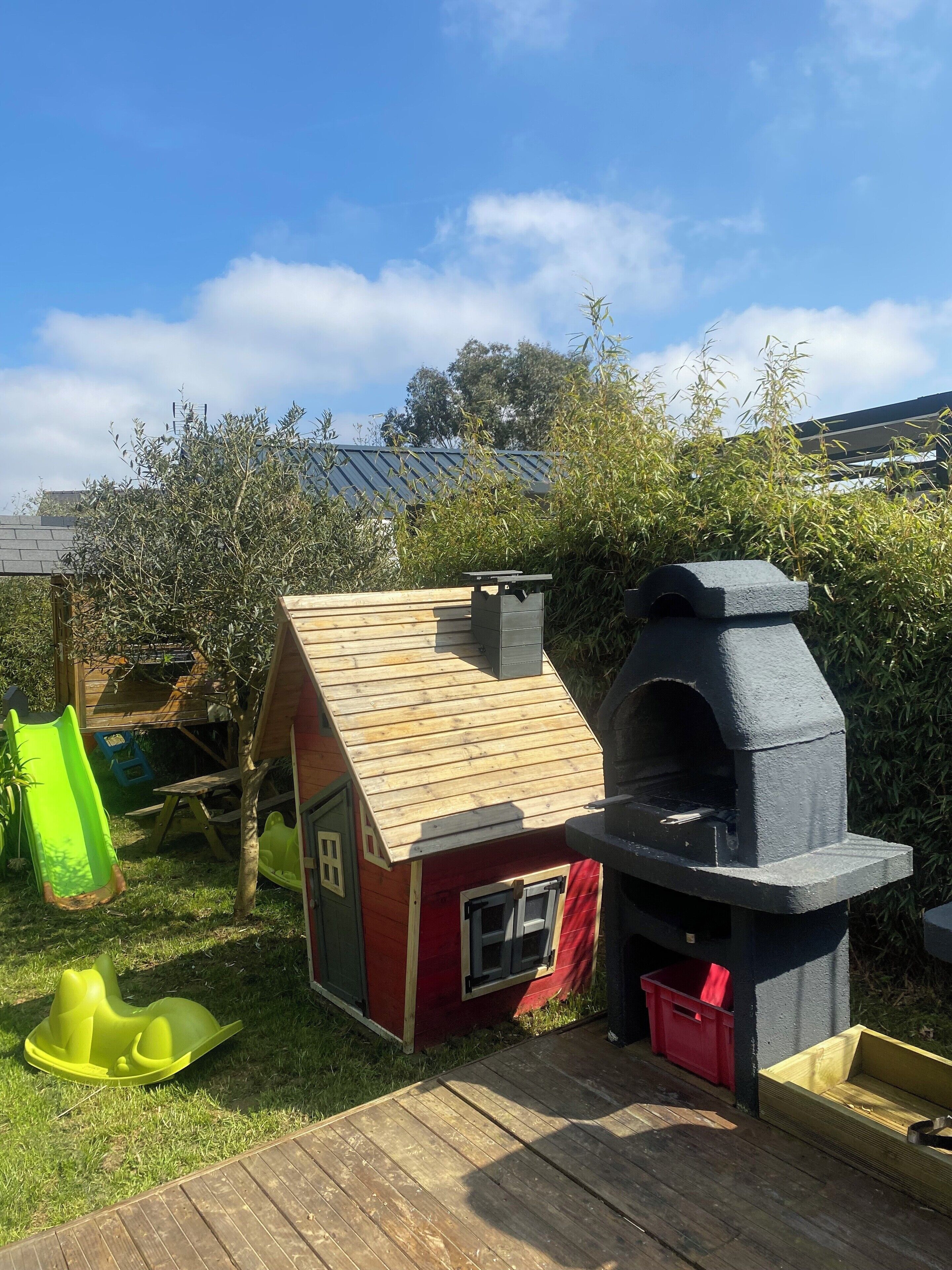 A wooden playhouse with a slide, a barbecue grill, and a small shed.