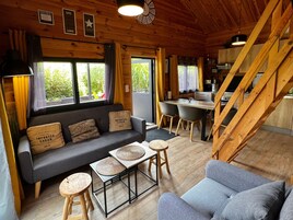 Interior acogedor de una cabaña con sofá, mesa de comedor, sillas, pisos de madera y una escalera.