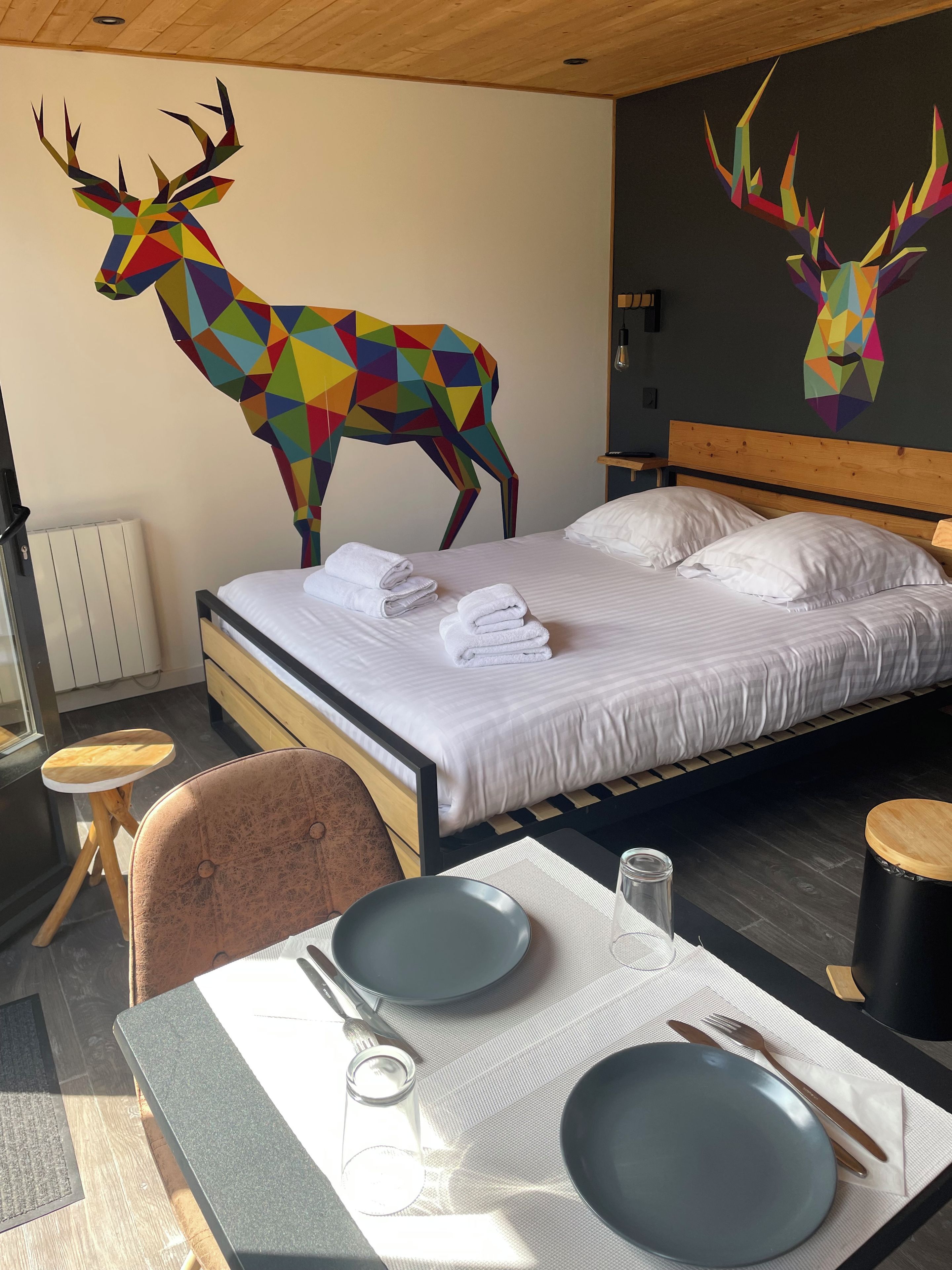 A hotel room with a bed, a table set for dining, and two deer wall art pieces.