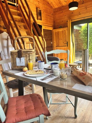 A wooden interior with a breakfast table set, a wicker basket, and a view of greenery outside. - Gites D'armor (Treguidel)