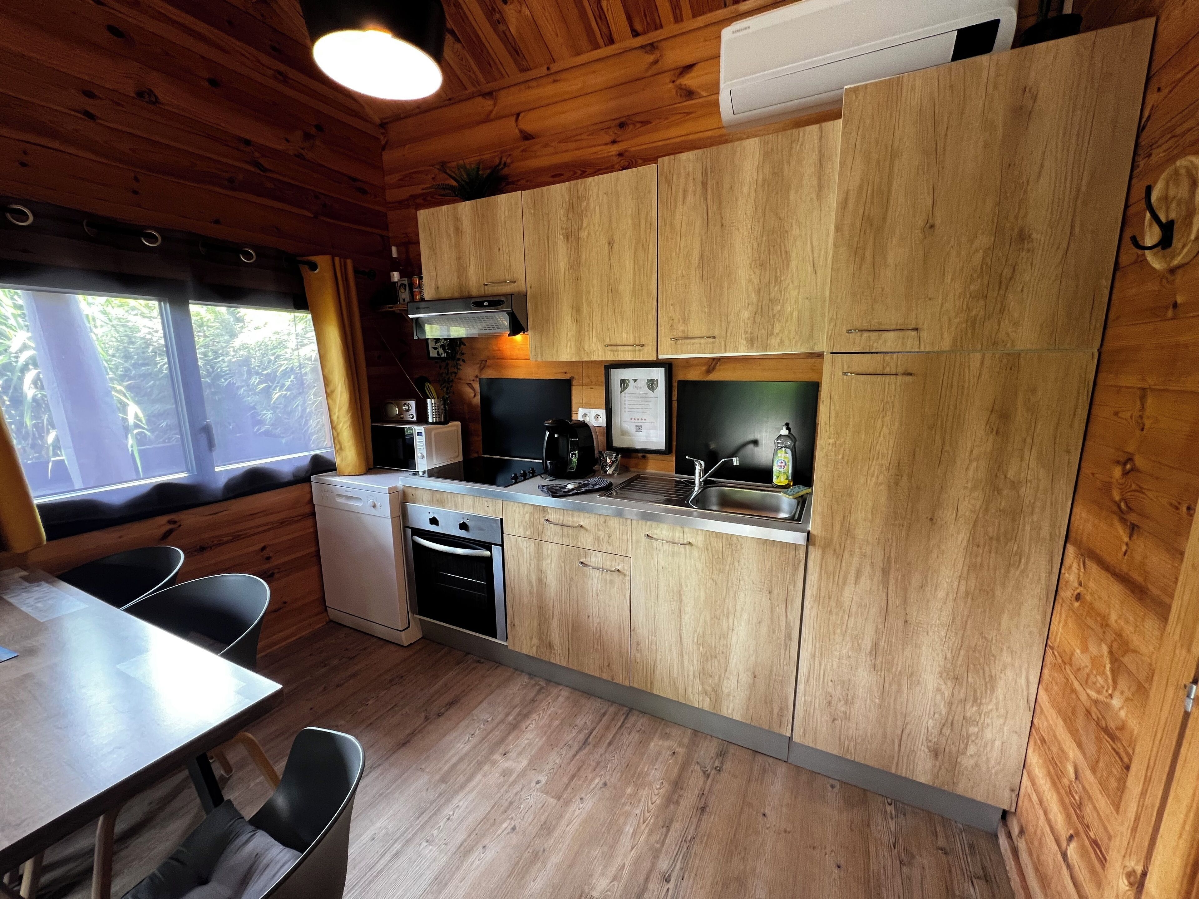 A compact kitchen with wooden cabinets, a built-in stove, a sink, and a window overlooking greenery.