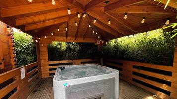A hot tub in a wooden cabin with a wooden ceiling and walls, surrounded by greenery.