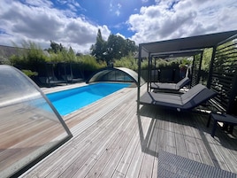 Una terraza de madera con piscina, sillas de descanso y un área de estar cubierta.