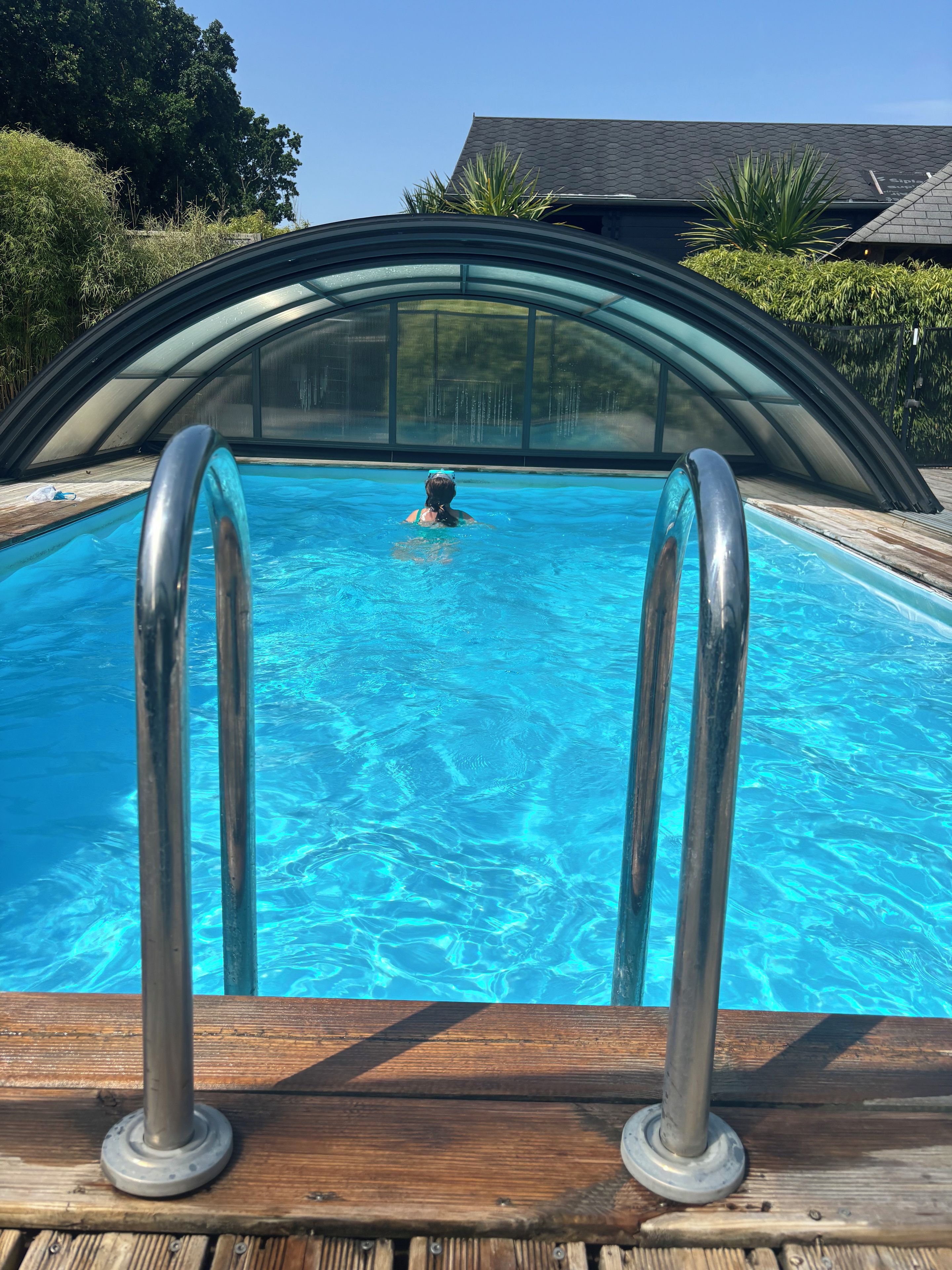 Une piscine à l’eau d’un bleu limpide, entourée d’une terrasse en bois et d’une rambarde métallique au bord du bassin.