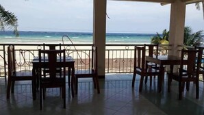 Un espace extérieur abrité, doté de tables et de chaises, offrant une vue sur une plage et l’océan.