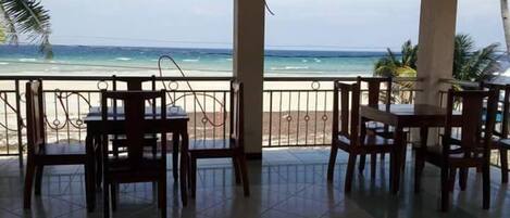 Un espace extérieur abrité, doté de tables et de chaises, offrant une vue sur une plage et l’océan.