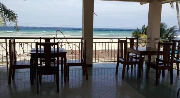 Un espacio de descanso al aire libre cubierto con mesas y sillas, con vistas a una playa y al océano.