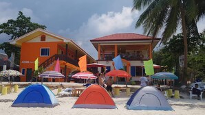 Une zone de plage avec des tentes et des parasols, un bâtiment avec un toit rouge et des palmiers.