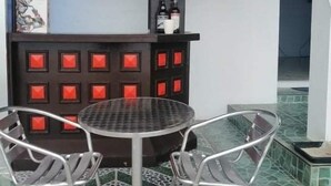 Un espace bar avec une table ronde et des chaises en métal, des étagères remplies de bouteilles et de verres, et un sol à motifs.
