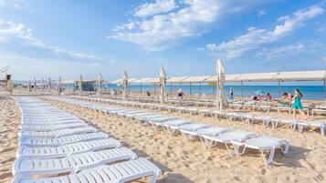 Een privéstrand, wit zand, ligstoelen aan het strand, parasols