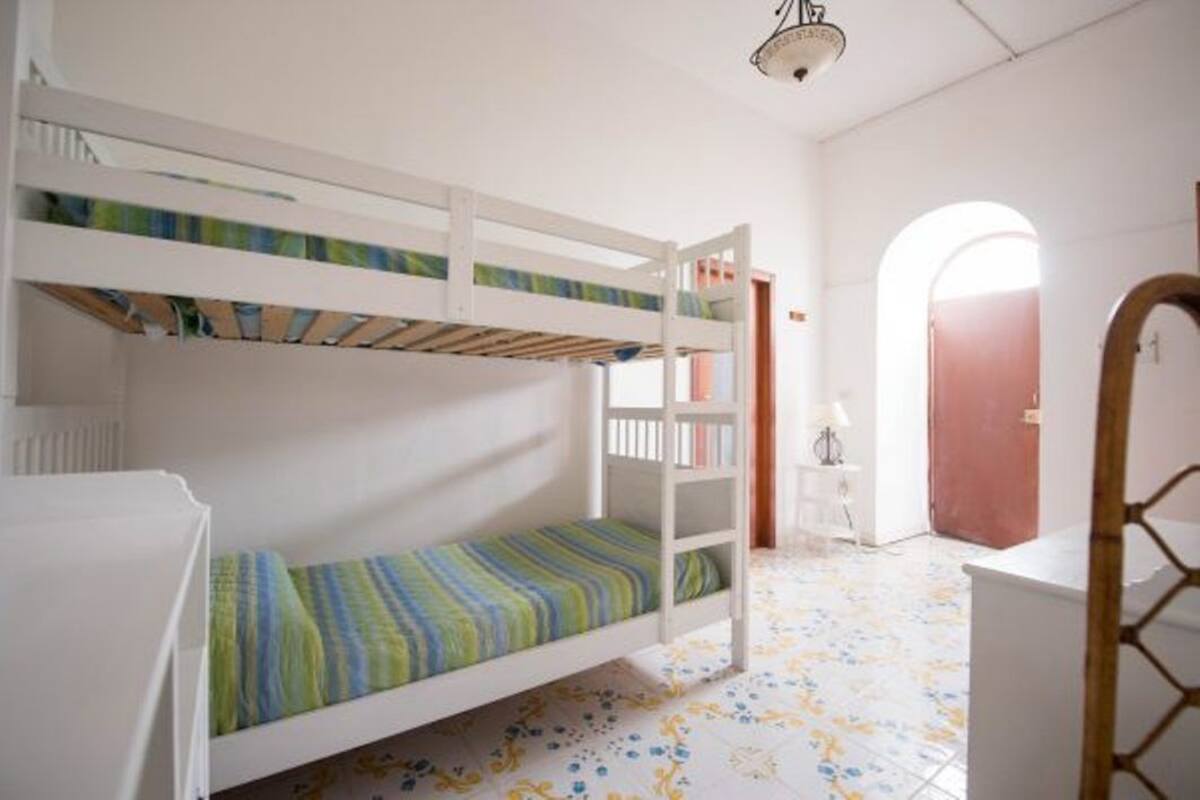 Ein Schlafzimmer mit Etagenbetten, einem weißen Deckenventilator, einem kleinen Tisch mit Lampe und einer Tür zu einem anderen Raum.