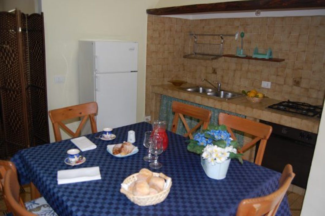 Un comedor con una mesa preparada para dos, una cocina con pileta y estufa, y un refrigerador.