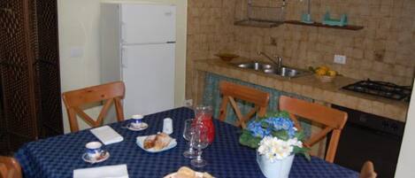 Un comedor con una mesa preparada para dos, una cocina con pileta y estufa, y un refrigerador.