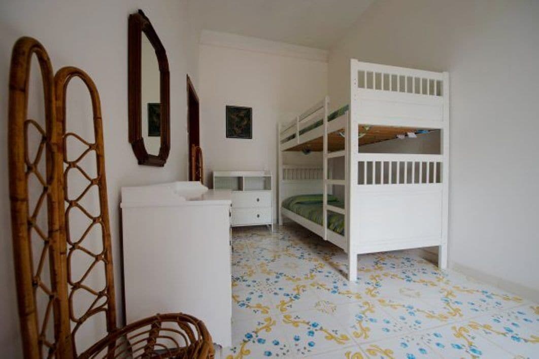 A bedroom with a bunk bed, a white dresser, a wicker chair, and a patterned floor.