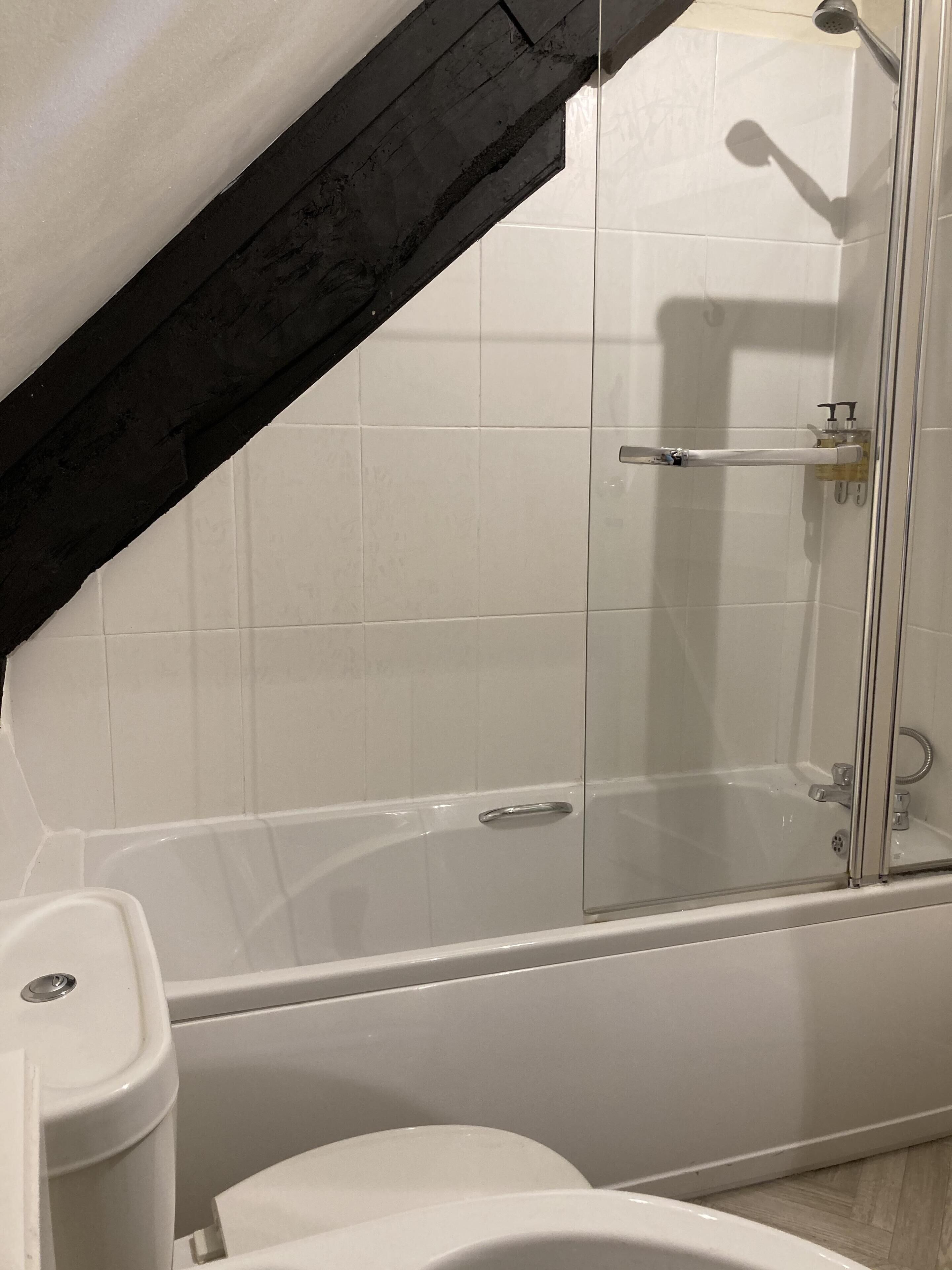 A modern bathroom with a glass-enclosed shower, white tiles, and a wooden beam structure.