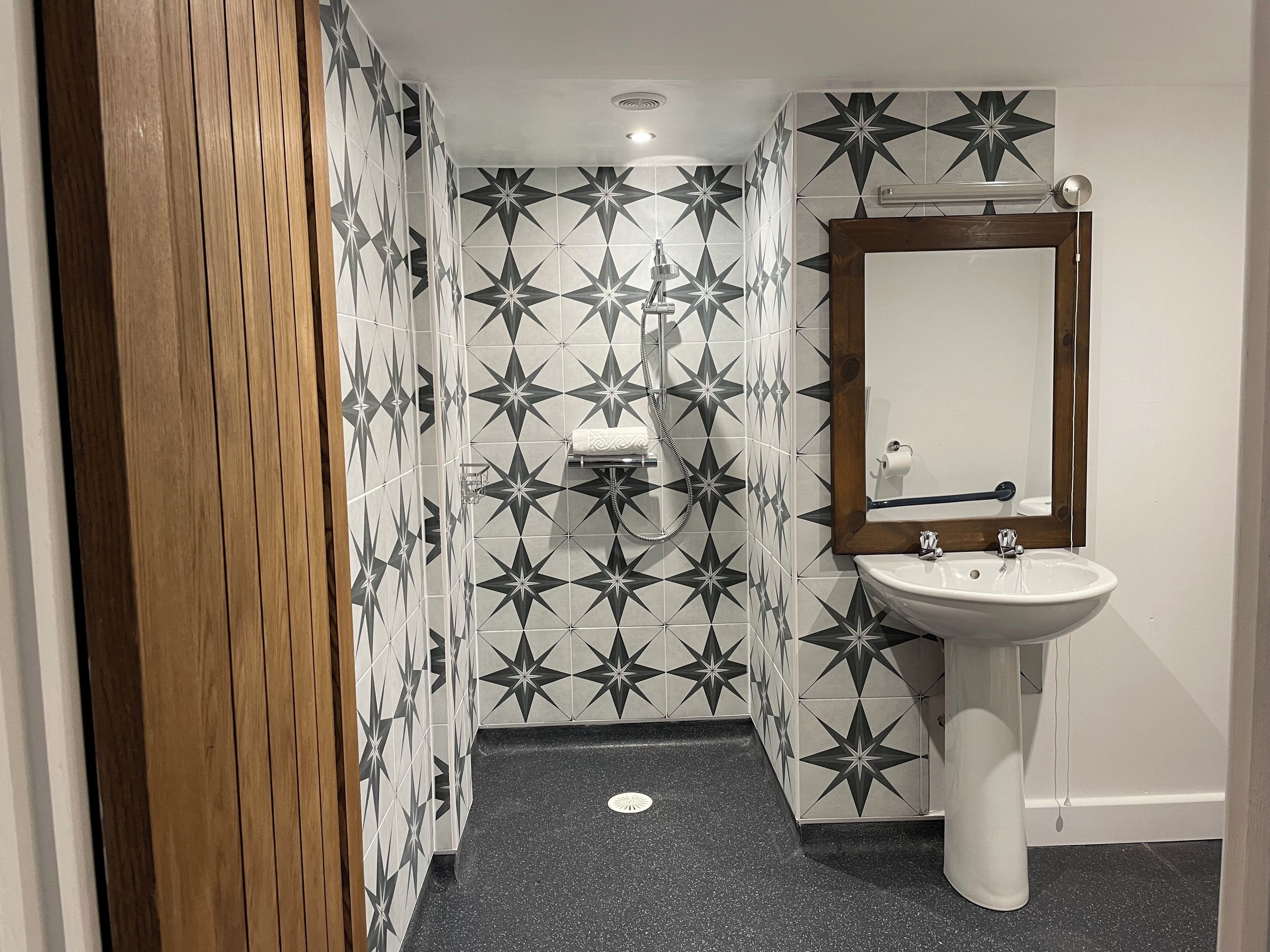 A bathroom with a star-patterned tile wall, a white pedestal sink, and a wooden door.