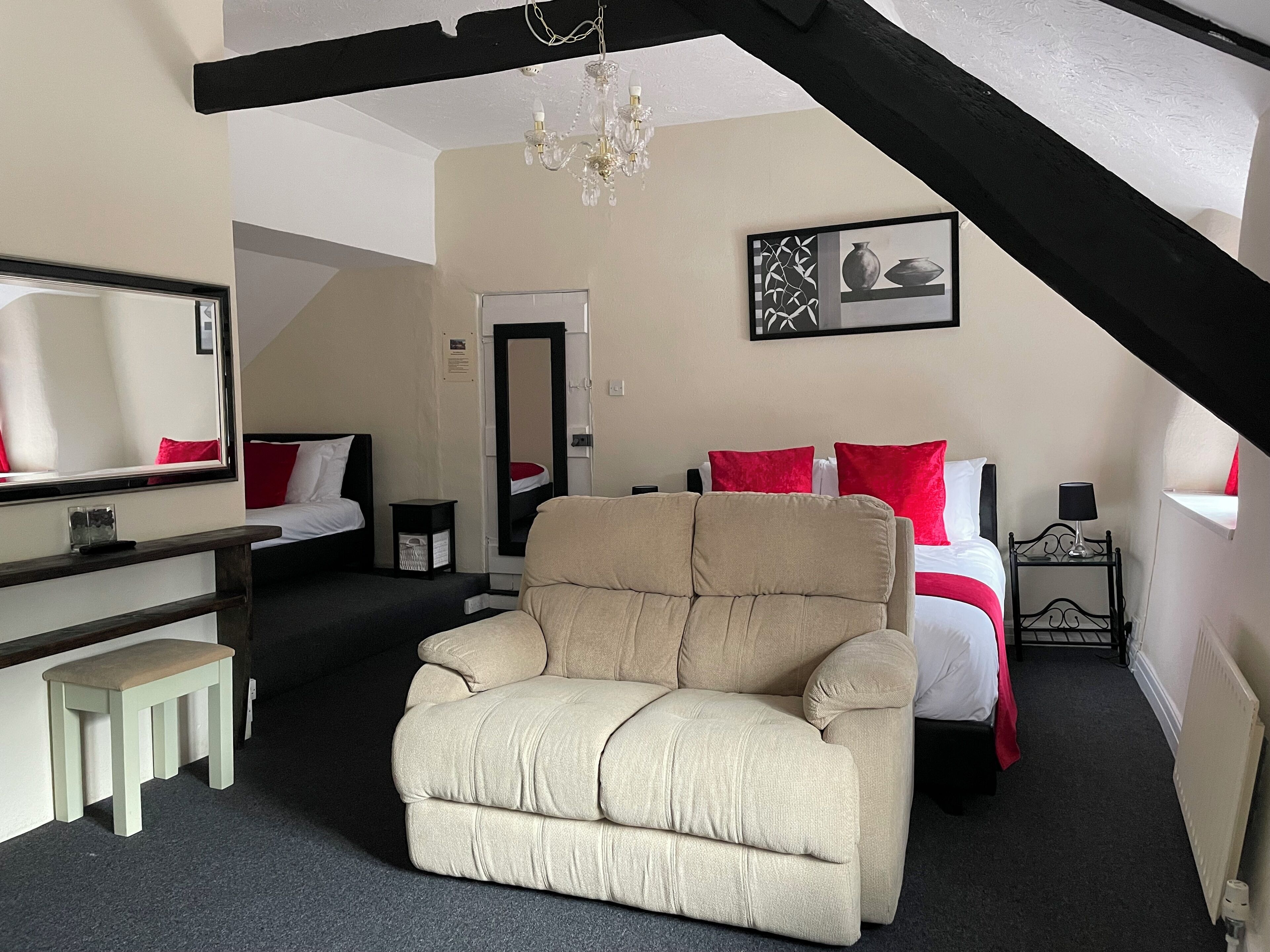 A hotel room with a bed, a chair, a desk, a mirror, a chandelier, and a painting on the wall.