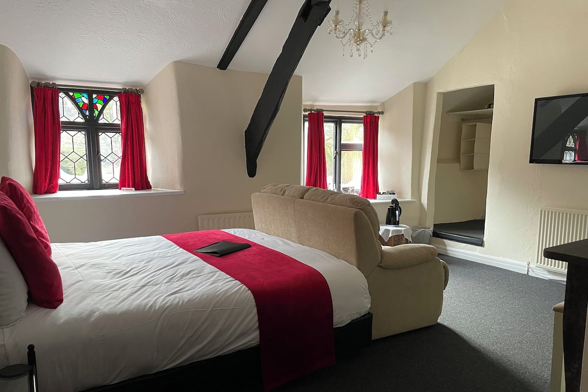 A hotel room with a bed, a chair, a TV, and a window with red curtains.