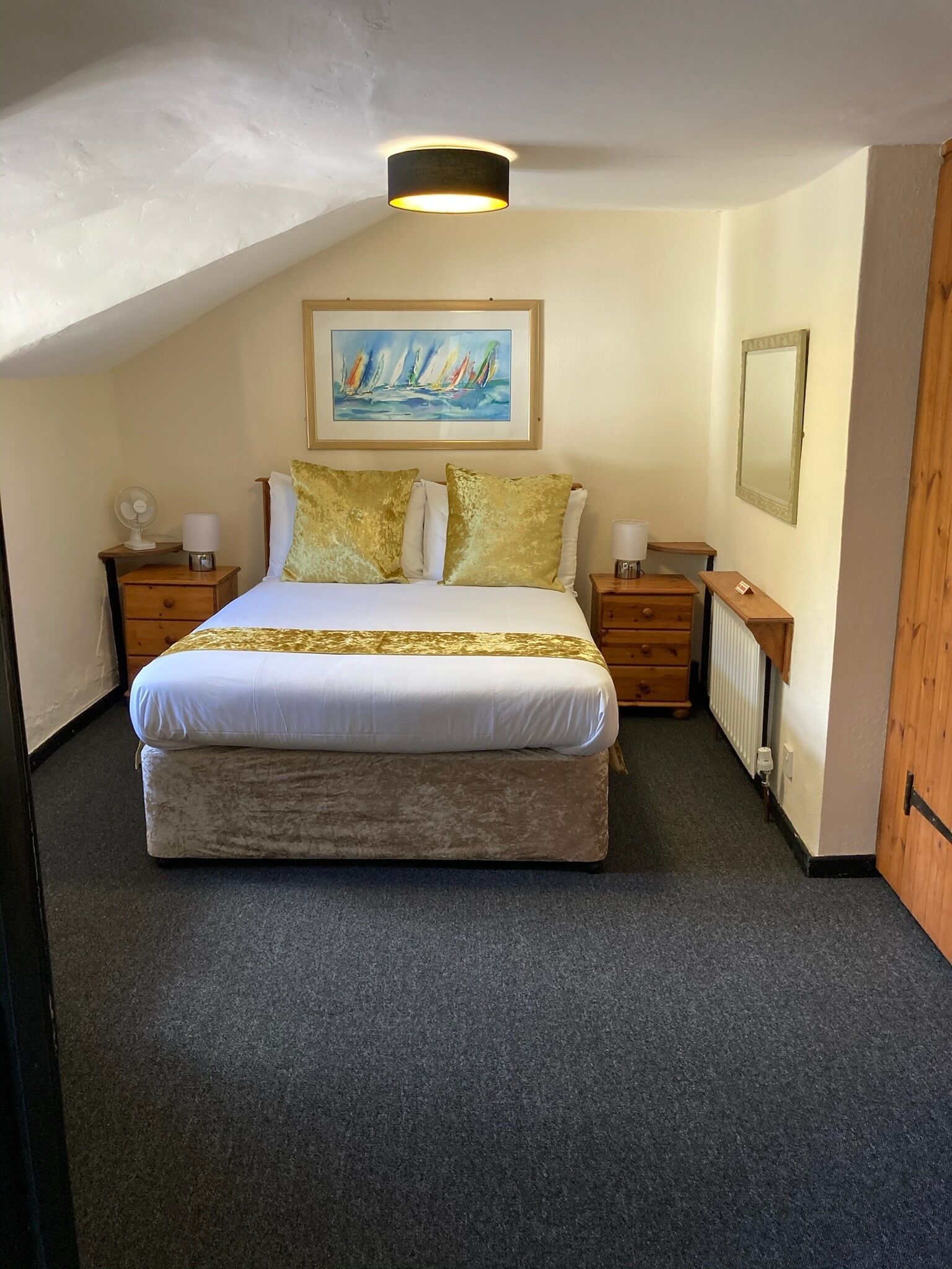 A bedroom with a bed, two nightstands, a painting, a mirror, and a radiator.